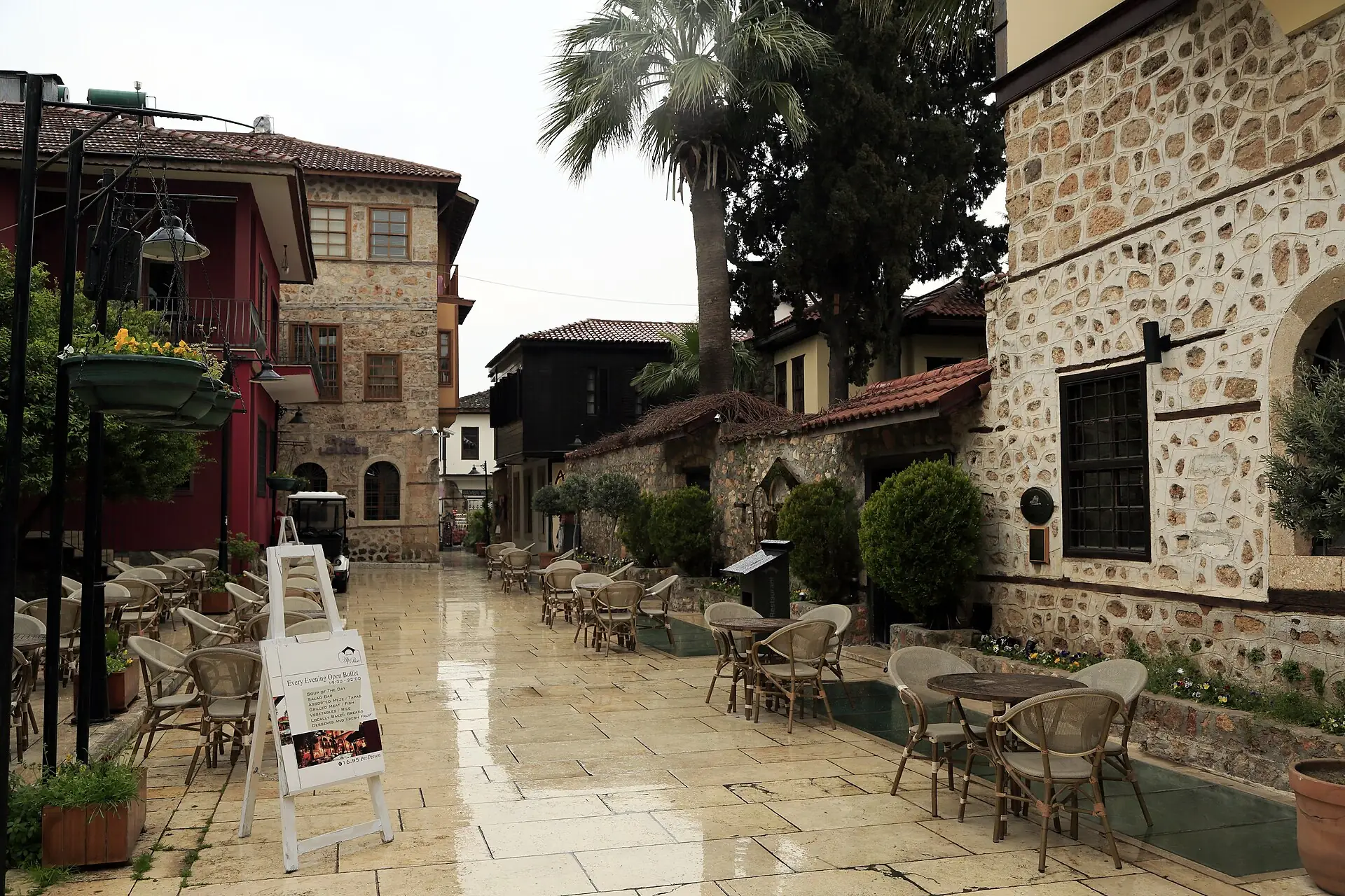 Hesapçı Sokak after rain: café chairs on wet stone paving, old stone houses and a palm tree